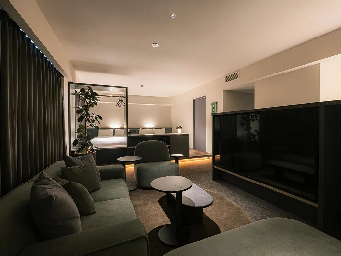 ソファと大型テレビ、コーヒーテーブルを配したリビング。奥のカーテン越しにベッドスペースが続く、広々とした一室。