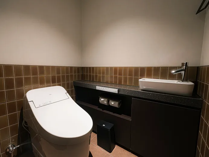 ウォシュレット付きトイレと洗面台を備えたタイル張りのバスルーム。