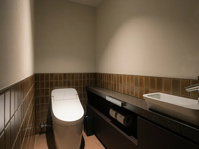 ウォシュレット付きトイレと洗面台を備えたタイル張りのバスルーム。