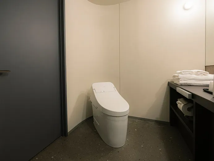 ウォシュレット付きトイレと、畳まれたタオルを置いた洗面カウンターを備えたバスルーム。