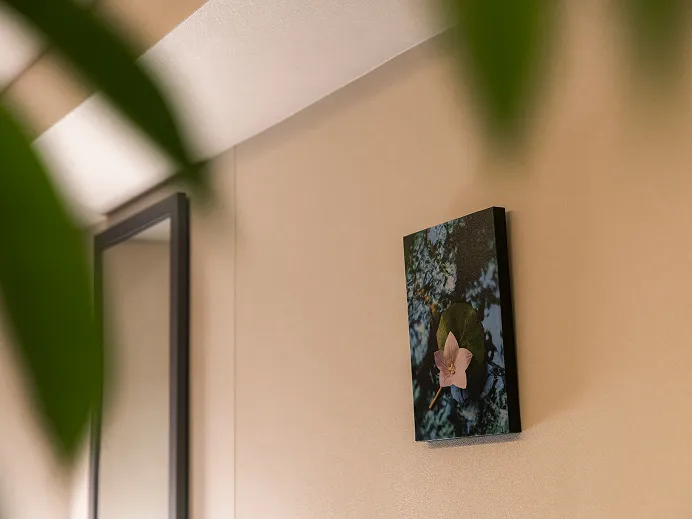 花を描いた絵画が飾られた壁。手前に観葉植物の葉がのぞく。