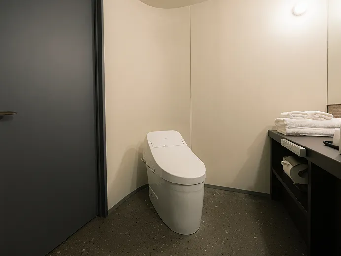 ウォシュレット付きトイレと、畳まれたタオルを置いた洗面カウンターを備えたバスルーム。